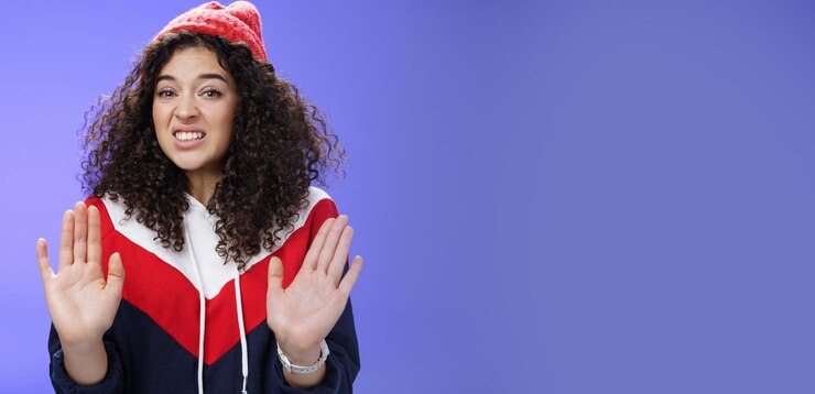 Free Photo displeased european woman with curly hair raising palms near chest and waving in refusal and rejecti