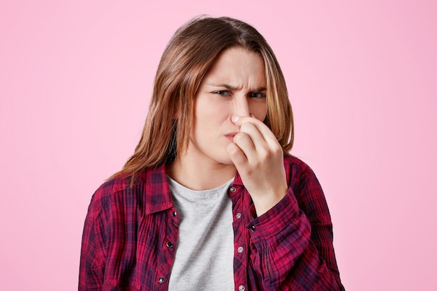 Displeased female model plugs nose as smells unpleasant scent