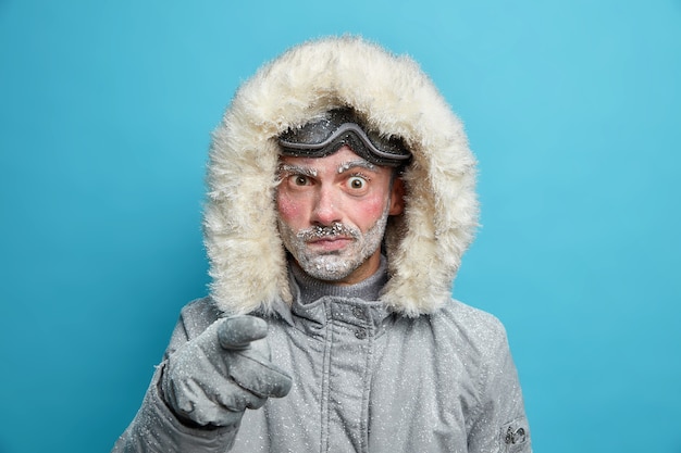 Free photo displeased frozen man with red face points in dissatisfaction blames you wears outerwear for cold weather prepares for winter adventure has active rest.