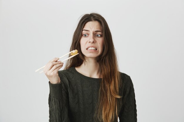 Displeased grimacing woman staring at tangerine on chopsticks