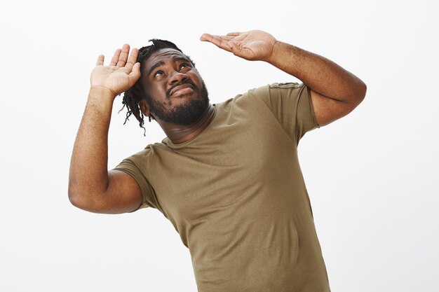 Displeased guy in a brown t-shirt posing against the white wall