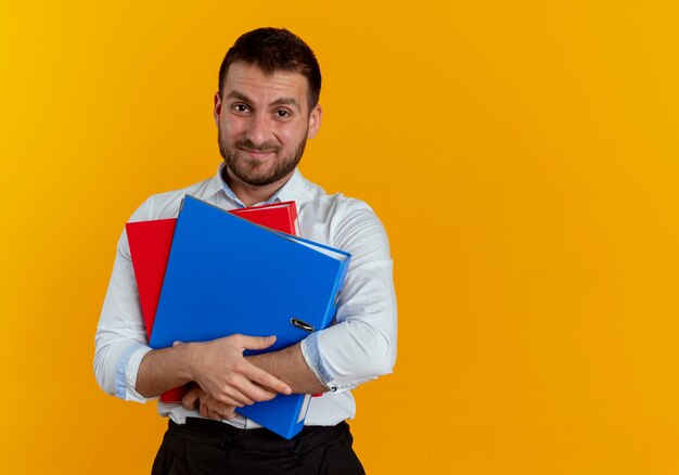 Displeased handsome man holds file folders isolated on orange wall