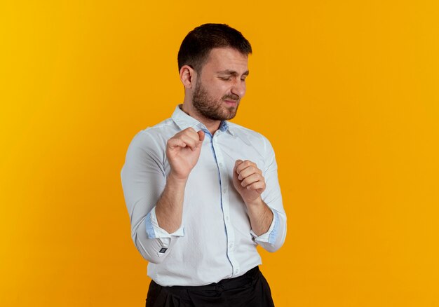 Displeased handsome man keeps fists with closed eyes isolated on orange wall