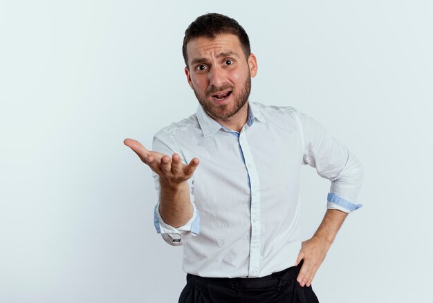 Displeased handsome man looks and points with hand isolated on white wall