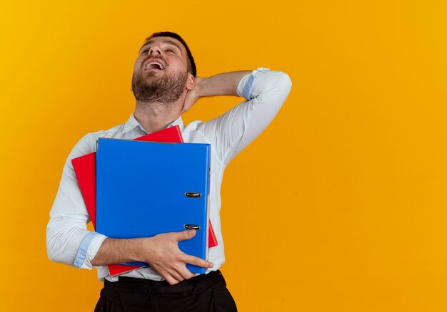 Foto gratuita uomo bello scontento mette la mano sulla testa dietro tenendo le cartelle di file isolate sulla parete arancione