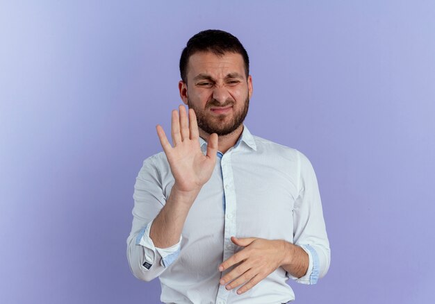 Displeased handsome man raises hand isolated on purple wall