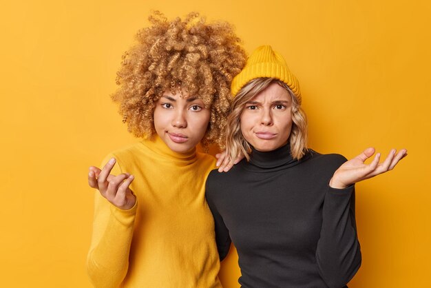 Displeased hesitant women keep palms raised shrug shoulders feel confused look questioned at camera wear casual black and yellow clothes cannot make decision People and uncertainty concept