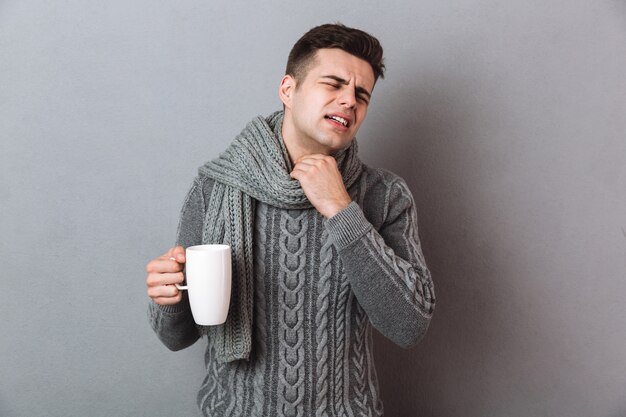 熱いお茶を保持している暖かいスカーフを着て不機嫌な病気の男。