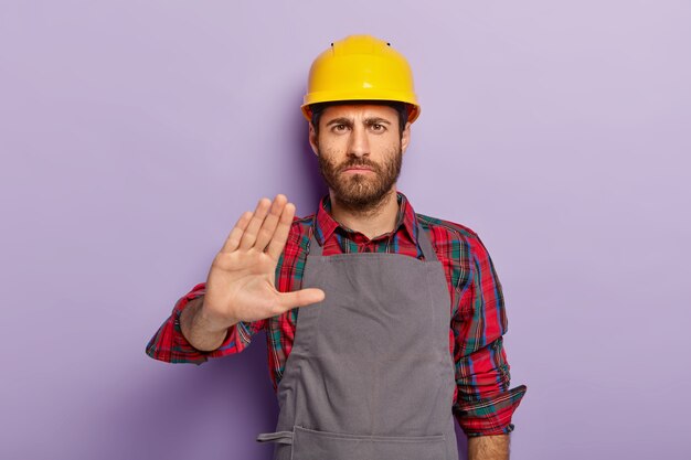 Displeased male engineer makes rejection gesture, says no, keeps palm outstretched at camera
