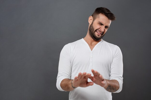 Displeased man refusing, stretching hands over grey wall