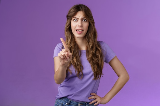 Displeased offended serious-looking assertive woman forbid express dislike and disapproval frowning annoyed shaking index finger prohibit refusing offensive behaviour stand purple background