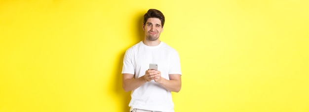 Free photo displeased and reluctant man grimacing being unamused by message on smartphone standing over yellow