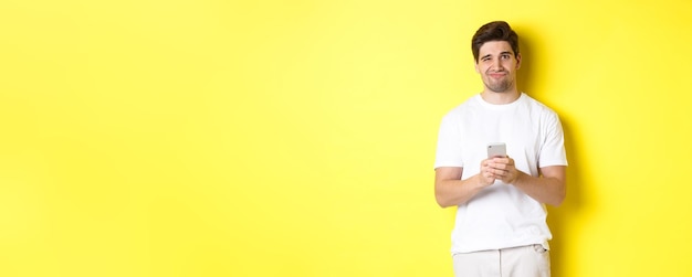 Free photo displeased and reluctant man grimacing being unamused by message on smartphone standing over yellow