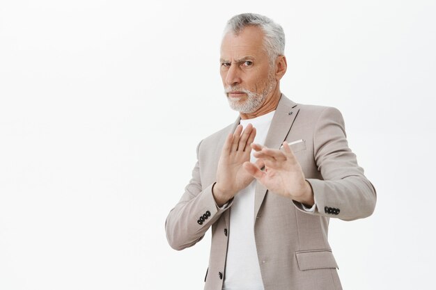 Displeased and reluctant senior man raising hands stop gesture, rejecting offer, white background