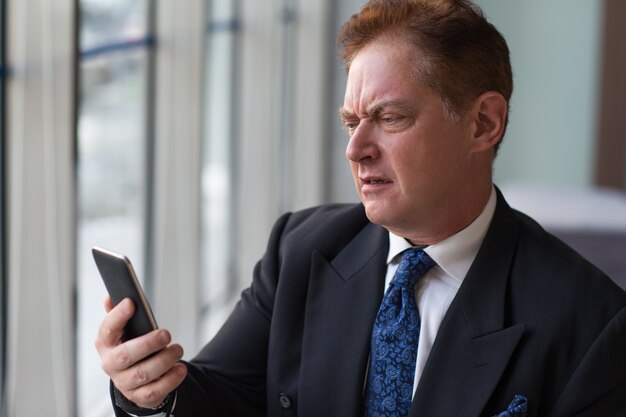 Displeased senior manager reading message on phone