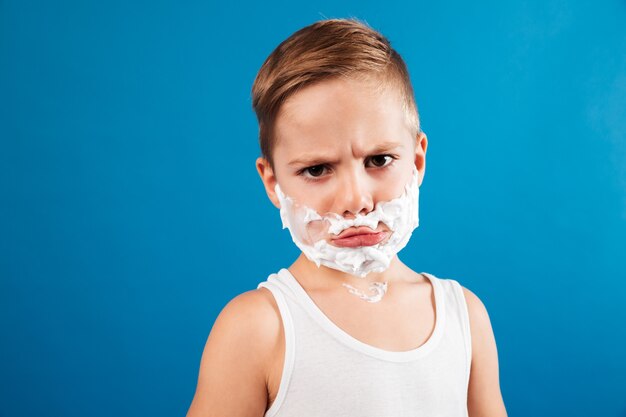 Недоволен серьезный молодой мальчик в пены для бритья, как мужчина