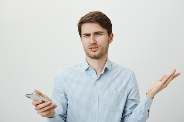 Displeased skeptical man spread hands sideways, reaction to app in mobile phone