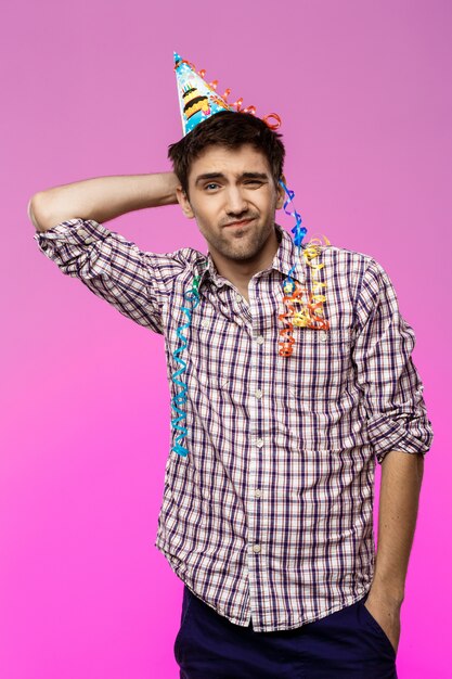 Displeased tired man at birthday party over purple wall.