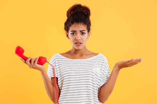 Displeased unhappy lady holding red handset while standing isolated