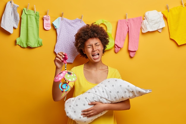 Free photo displeased upset mother being tired of nursing baby infant, holds mobile, tries to sooth crying newborn, busy with domestic chores and babysitting, poses