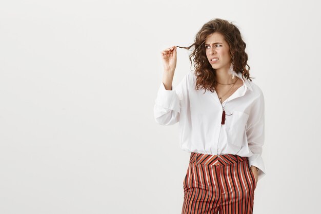 Displeased woman looking at hair strand, need new haircut