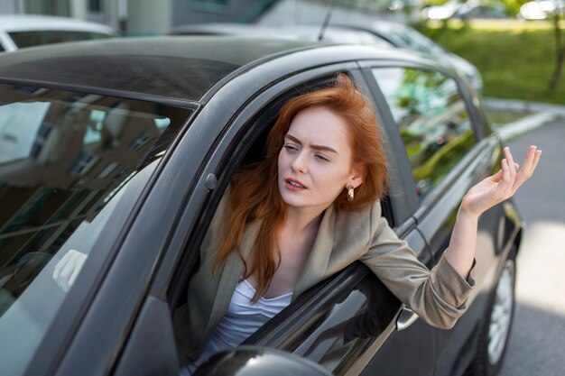 ぼやけた前景で車を運転している間、サイドウィンドウから外を見て、手で指している不機嫌な女性