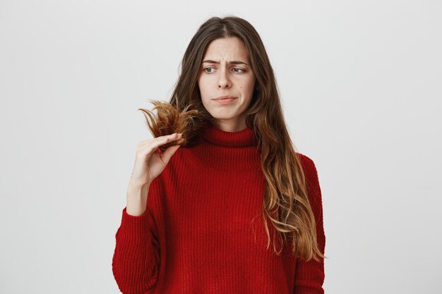 Displeased woman looking at split ends of hair