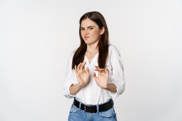 Displeased woman showing stop, rejection gesture, waving hands to decline, refuse of something ugly, standing over white background.