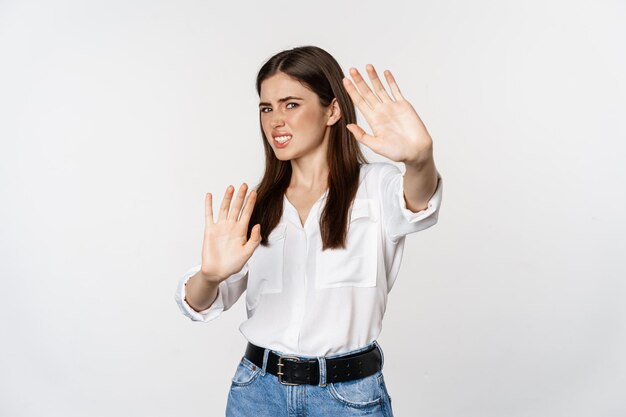 Недовольная женщина показывает стоп, жест отказа, машет руками, чтобы отказаться, отказывается от чего-то уродливого, стоит на белом фоне
