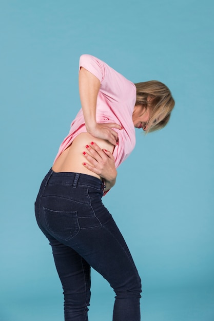 Displeased woman suffering from lower back pain on blue background