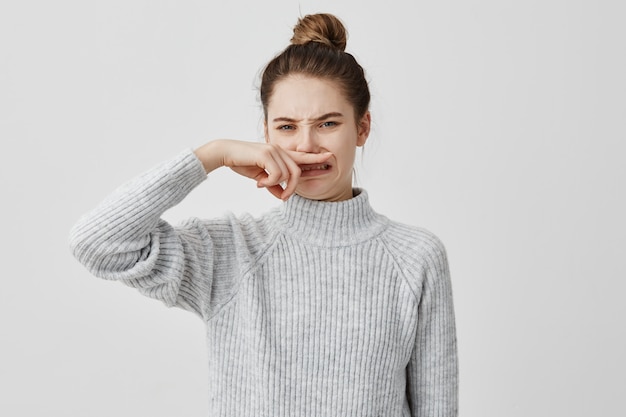 Displeased woman wearing casual closing nose with index finger looking with disgust. Young female blogger smelling something unpleasant while working in cafe. Bad smell concept