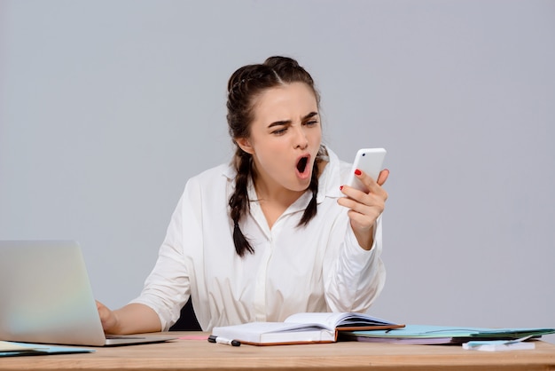 Displeased young beautiful businesswoman looking on phone at workplace