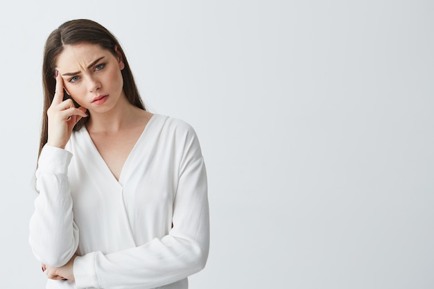 Displeased young beautiful businesswoman thinking with finger near temple .