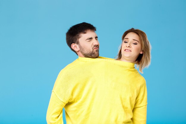 파란색에 포즈를 취하는 노란색 스웨터를 입은 불쾌한 젊은 아름다운 커플