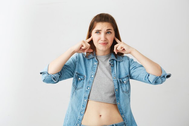 Displeased young beautiful girl closing ears with fingers over white background