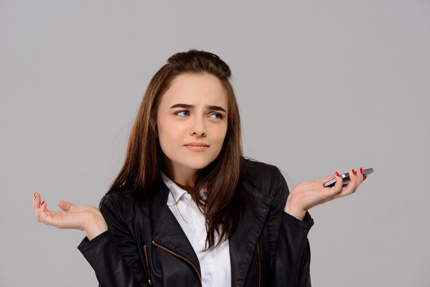 Free photo displeased young beautiful woman holding phone over purple wall