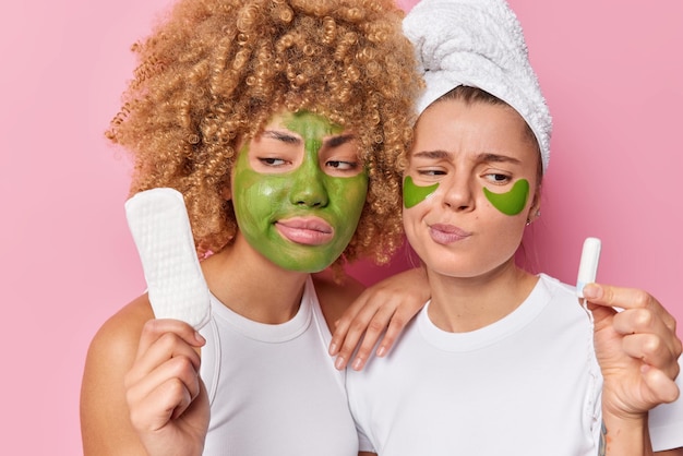 Free photo displeased young beautiful women hold sanitary napkin and tampon choose product for menstruation apply green beauty patches and moisturising mask isolated over pink background hygiene concept