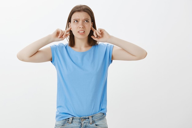 Недовольная молодая студентка жалуется на шумных соседей, закрывает уши пальцами