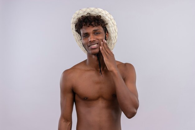 太陽の帽子をかぶっている巻き毛の不機嫌な若いハンサムな浅黒い肌の男