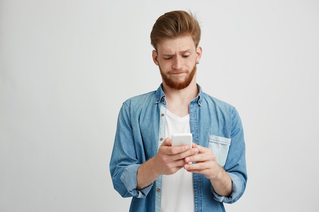 Displeased young handsome guy looking at phone screen browsing web.