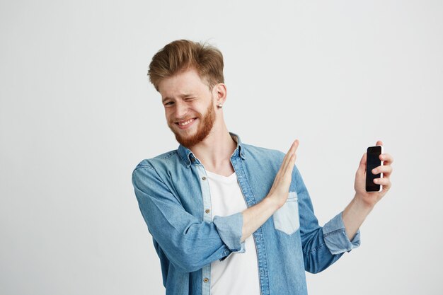 Displeased young handsome man showing stop sign to phone in another hand resisting.