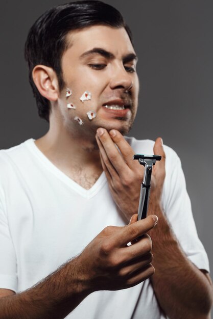 Displeased young handsome man touching face after shaving on grey