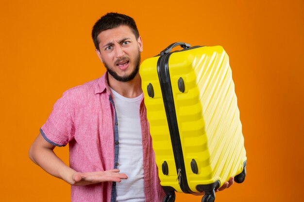 不機嫌な若いハンサムな旅行者の男のスーツケースを持ってイライラして立っている彼のスーツケースに手の腕で指しているイライラ