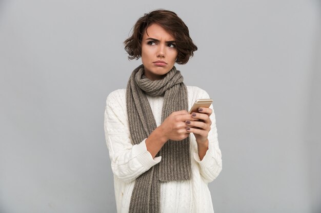 携帯電話でチャットスカーフを着て不機嫌な若い女性。