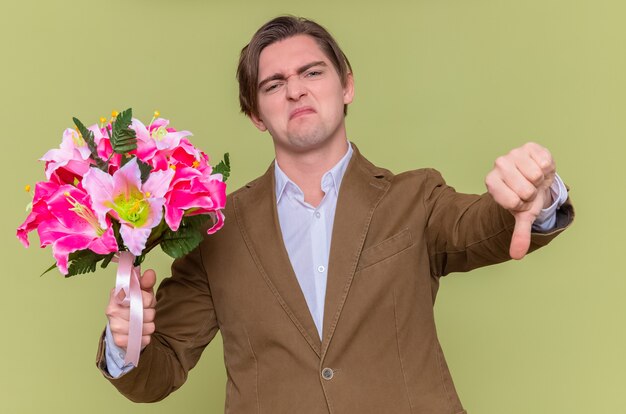 Недовольный молодой человек, держащий букет цветов, показывает палец вниз