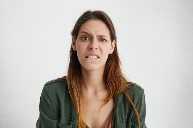 Foto gratuita giovane donna graziosa scontenta che curva le sue labbra, morde con i denti, fronte accigliato che guarda con disappunto avendo alcuni fallimenti. donna carina con viso ovale, capelli tinti scuri in abiti casual