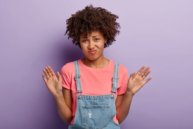 Displeased young woman with an afro posing in overalls