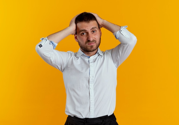 Displesed handsome man holds head looking isolated on orange wall