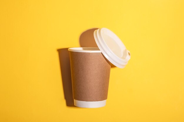 Disposable paper cup with a dark shadow on a yellow background top view