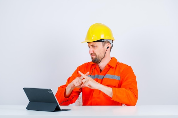 Dissatisfied architect is crossing fingers by looking at tablet on white background